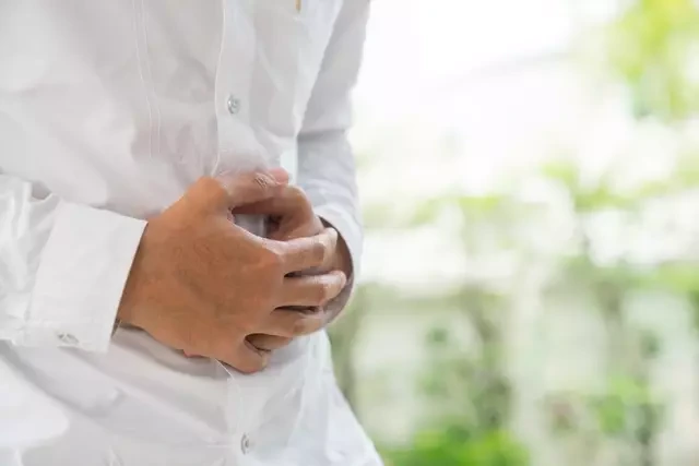 Man clutching his stomach in discomfort, a common early symptom of liver strain or digestive issues.