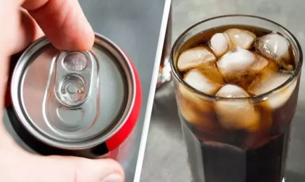 Close-up of an opened soda can beside a glass filled with cola and ice cubes.